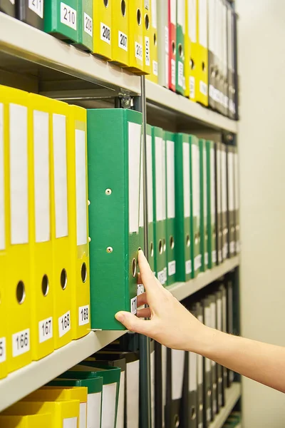 Yellow and green file folders in archive and human hand