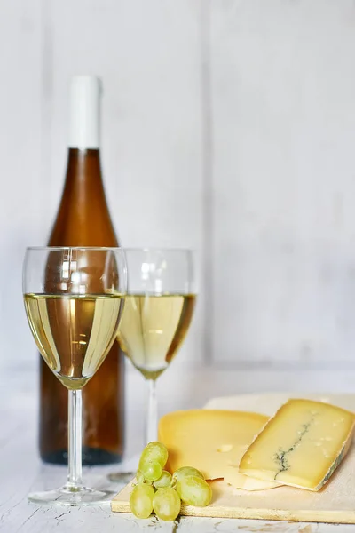 Garrafa e dois copos de vinho branco, uva branca e queijo azul em um fundo de madeira — Fotografia de Stock