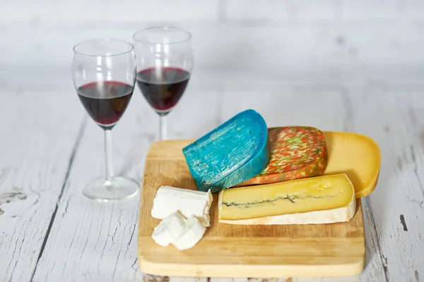 Dois copos de vinho tinto e variação de queijo em tábua de madeira — Fotografia de Stock