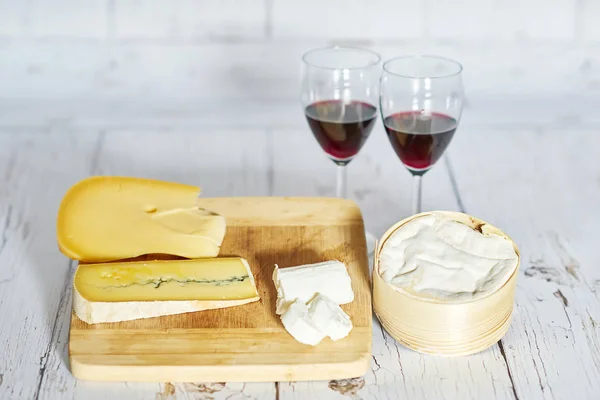 Dois copos de vinho tinto e placa de queijo na bandeja de madeira — Fotografia de Stock