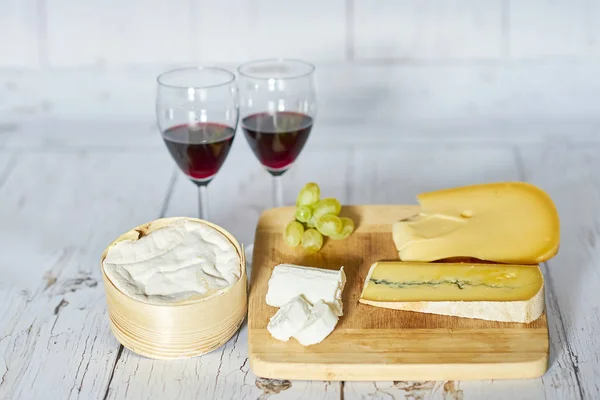 Dois copos de vinho tinto e placa de queijo na bandeja de madeira - horizontal — Fotografia de Stock