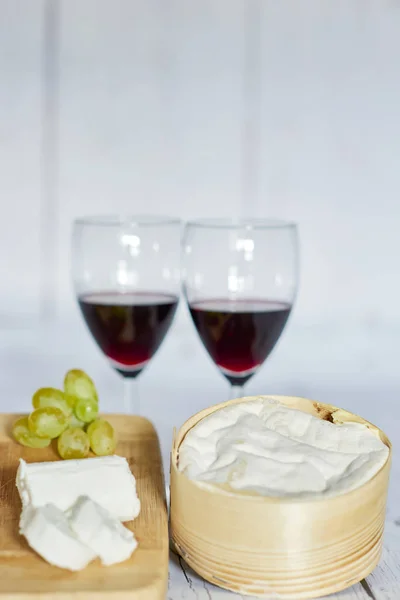 Dois copos de vinho tinto e placa de queijo na bandeja de madeira - vertical — Fotografia de Stock