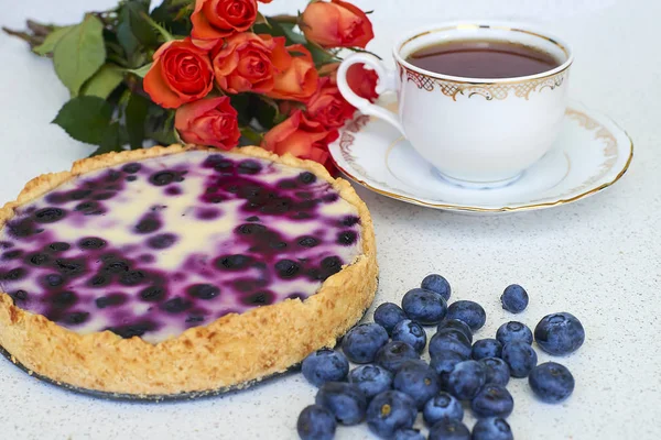 Böğürtlenli turta, fincan çay, yaban mersini ve beyaz zemin üzerine kırmızı gül yığını 