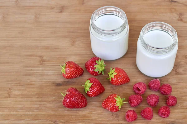 Dois frascos de vidro com iogurte, framboesas e morangos vista horizontal de alto ângulo — Fotografia de Stock