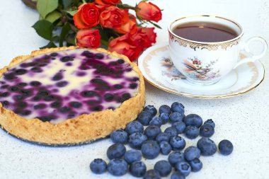 Böğürtlenli turta, fincan çay, yaban mersini ve kırmızı gül beyaz bir arka planda - natürmort yiyecek yığını 