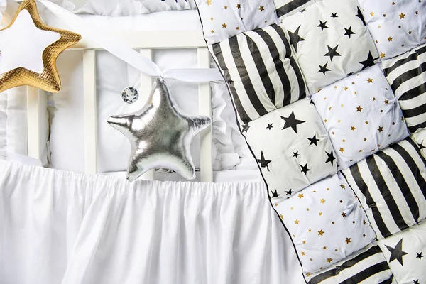 Almohadas en forma de estrella de plata y oro y edredón patchwork en una cuna blanca de cerca —  Fotos de Stock