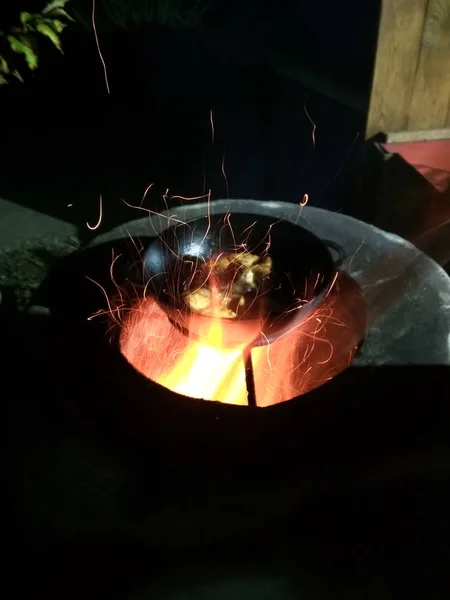 Voedsel koken in wok boven open vuur in tandyr oven buitenshuis in de nacht met vuur knippert. — Stockfoto