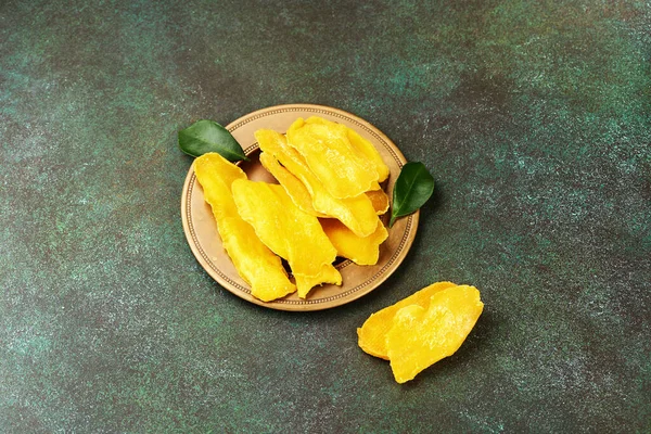 Dried mango fruit with fresh leaves on green background. Yellow sliced mango.