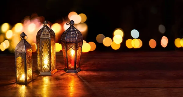 Ramadan lanterns on the table. Dark background with street light and bokehs. Beautiful Greeting Card with copy space for Ramadan and Muslim Holidays. An illuminated Arabic lamp. Mixed media.