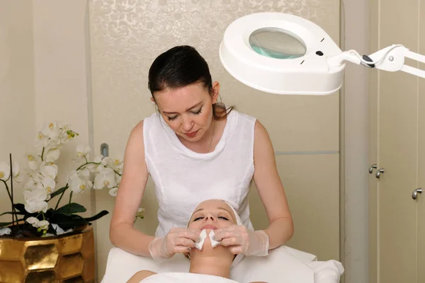 beautician doing facial skin procedure for young women laying down in a beauty salon