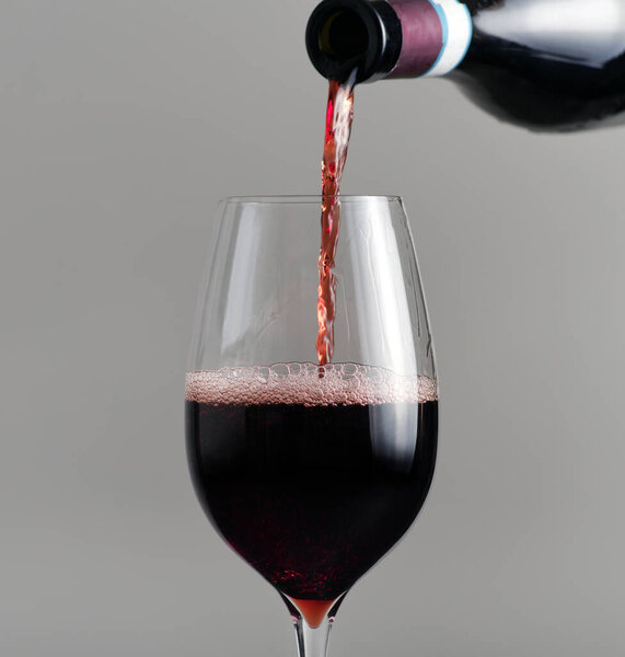 Pouring red wine from bottle into glass close up