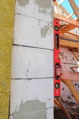 Yeni beyaz tuğla duvar kontrol etmek için bir ruh düzeyi kullanarak Duvarcı ustası. Örmek temelleri duvar Techniques.Roofing inşaat. Ahşap inşaat. yalıtım yün montajı. Beyaz yapı taşları