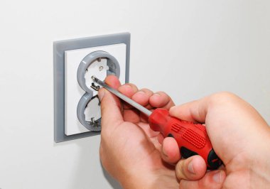 Beyaz bir duvar, bir tornavida ile gri bir duvara monte edilmiş Ac elektrik prizine yüklemek elektrikçi Ev Tadilatı.