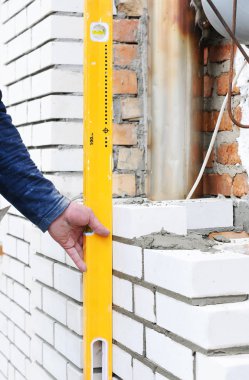 Yeni beyaz tuğla duvar açık kontrol etmek için bir ruh düzeyi kullanarak çimento. 