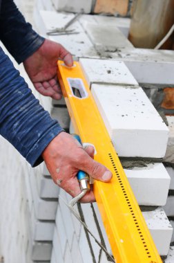 Yeni beyaz tuğla duvar açık kontrol etmek için bir ruh düzeyi kullanarak çimento. 