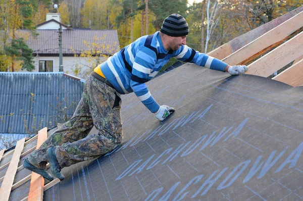 Trabajador de la construcción instala barrera de vapor en el techo. techo en construcción. alpinista constructor utiliza una grapadora para sujetar la barrera de vapor y la impermeabilización . — Foto de Stock
