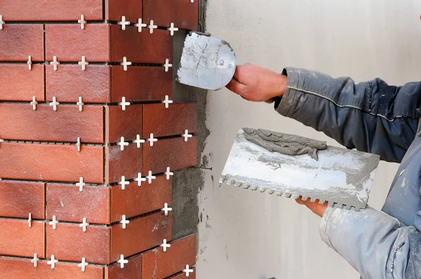 Tiler construction worker installing decorative tiles on the facade of the building. Insulated and plastered facade.