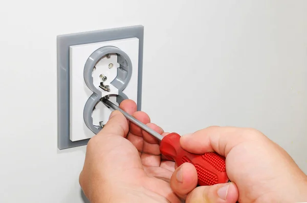 Electricista instalando un enchufe de corriente alterna gris montado en la pared con un destornillador en una pared blanca, renovando el hogar . — Foto de Stock