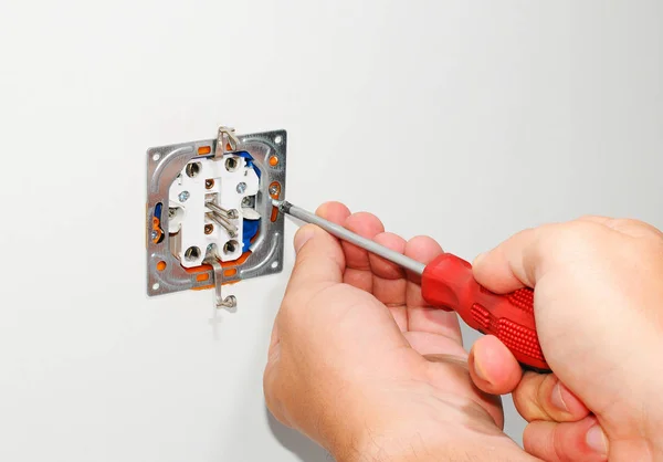 Electricista instalando un enchufe de corriente alterna gris montado en la pared con un destornillador en una pared blanca, renovando el hogar . — Foto de Stock