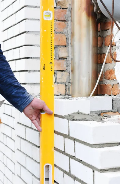 Yeni beyaz tuğla duvar açık kontrol etmek için bir ruh düzeyi kullanarak çimento. 