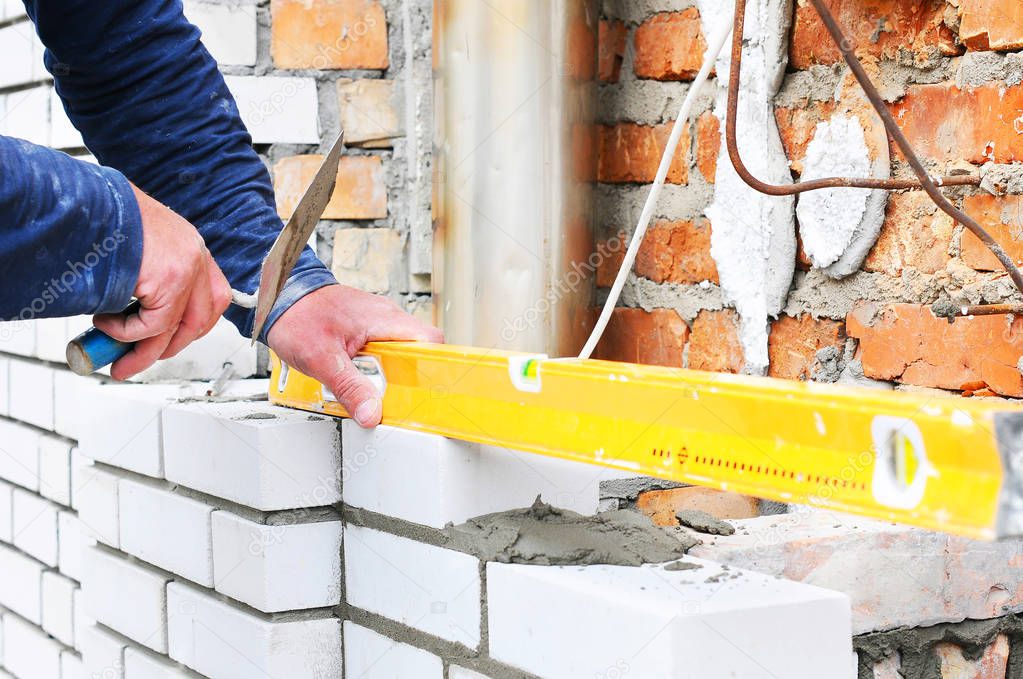 Bricklayer Using a Spirit Level to Check New White Brick Wall Outdoor. 
