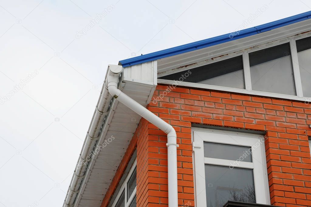 White gutter on the roof top of house. The red brick house with large Windows close up