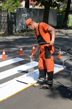 Irpin, Ukrayna - 06 Mayıs 2017: Çalışan bir yaya yaya geçidi boyuyor. Boyama ve asfalt yüzeyine boya püskürtme tabancası kullanarak satırlarda yaya geçidi yatacak teknik yol adam işçi.