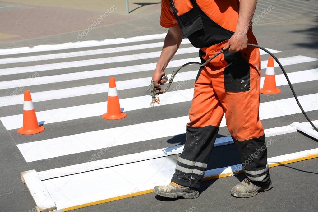 Worker is painting a pedestrian crosswalk. Technical road man worker painting and remarking