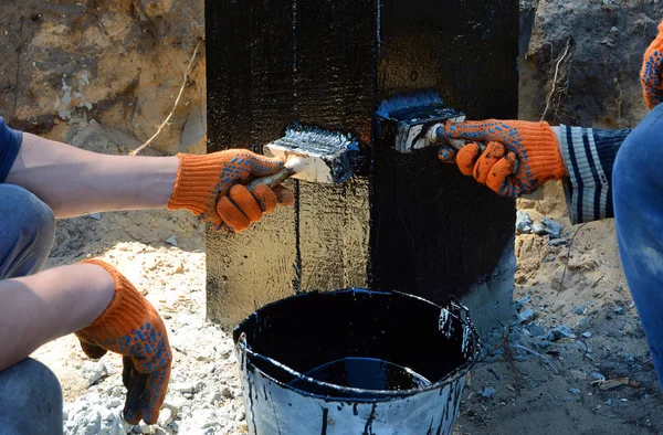 Trabajadores contratistas pintando alquitrán de carbón negro o betún en la superficie de hormigón por el cepillo, Una impermeabilización. Impermeabilización de cimientos, recubrimientos a prueba de humedad . — Foto de Stock