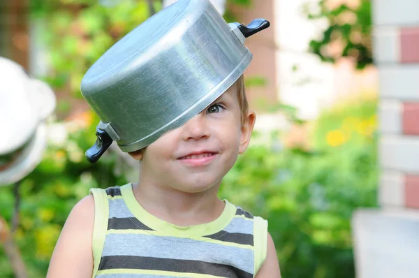 Un niño pequeño con una cacerola en la cabeza. niño con una cacerola. El niño feliz se complace. Un niño con un sombrero de cacerola . — Foto de Stock