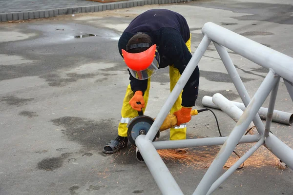 Trabajador que usa amoladora eléctrica Aserrado de metal con chispas intermitentes. El trabajador corta un trozo de tubo de la estructura metálica . — Foto de Stock