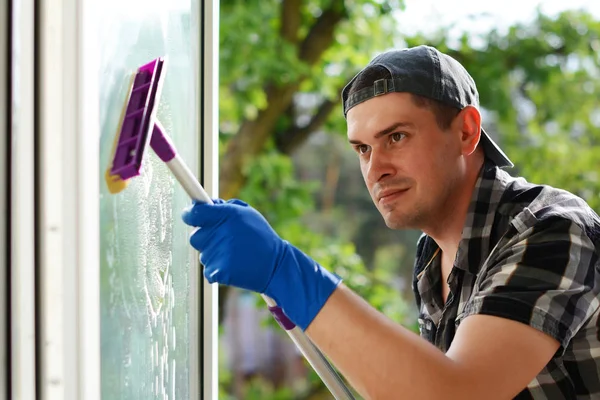 Mladý muž čištění okna s mopem. Ostřikovač okna. Profesionální úklidová firma. — Stock fotografie