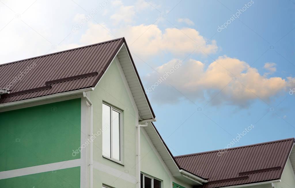 White gutter on the roof top of house. Metal roofing. Roof Snow Guards. Roof protection from snow board (Snow guard) on house construction. Modern house against the blue sky.