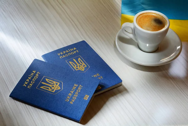 Bir fincan kahve ve bir pasaport. Yeni Ukrayna mavi biyometrik pasaport ile kimlik çipi ahşap arka plan üzerinde — Stok fotoğraf
