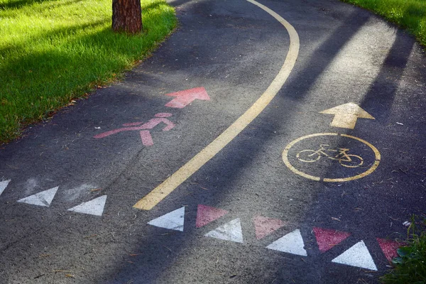A calçada e ciclovia. Sinal de bicicleta amarela na faixa de bicicleta de asfalto no parque da cidade no fundo . — Fotografia de Stock