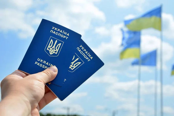 Novo passaporte biométrico azul ucraniano com chip de identificação no céu azul e fundo de bandeira ondulada. A mão de um jovem tem um passaporte biométrico ucraniano — Fotografia de Stock