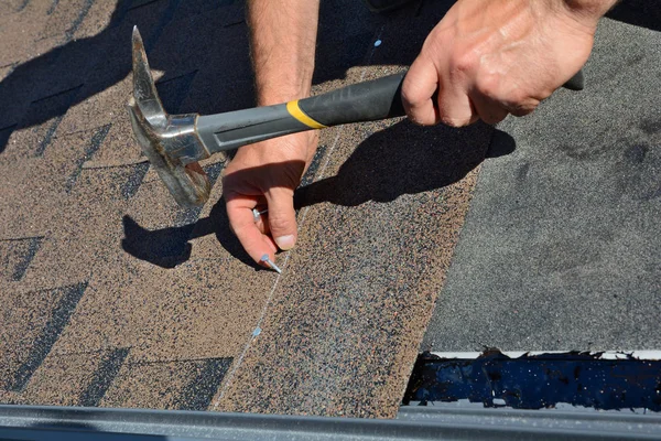 Arbetaren händerna installera bitumen tak bältros. Arbetaren hammare i naglar på taket. Roofer hamrar en spik i tak bältros. Ofärdiga taket. — Stockfoto