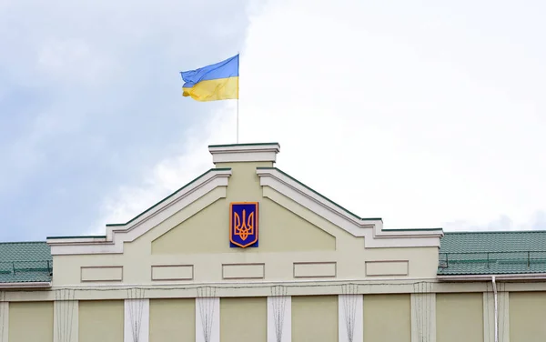 Ukrainian flag on the flagpole flies against a sky. Ukrainian flag on the building and a sign of the trident as a symbol of Ukraine