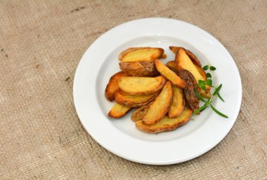 Kızarmış patates dilimleri plaka üzerinde otlar ile.