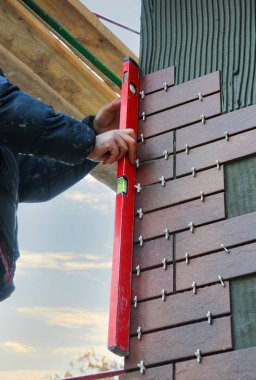 İnşaat işçisi binanın cephesinde dekoratif karolar kontrol etmek için bir ruh düzeyi kullanın.