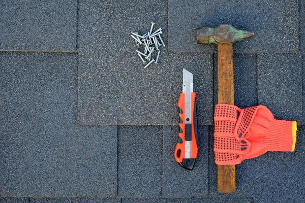 Close up view on asphalt shingles on a roof  with hammer,nails and knife. Use of gloves in construction