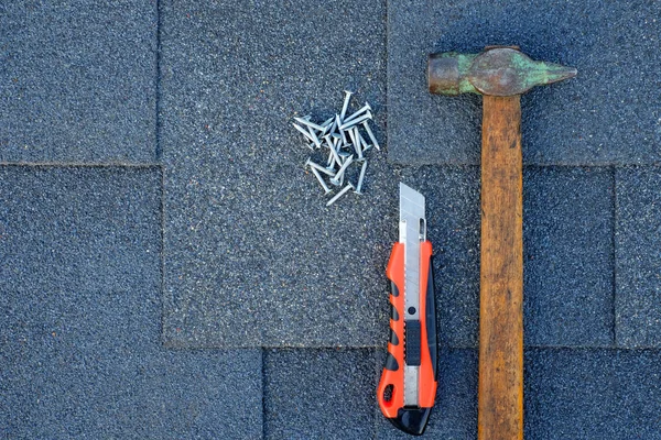 Close up view on asphalt shingles on a roof  with hammer,nails and stationery knife.