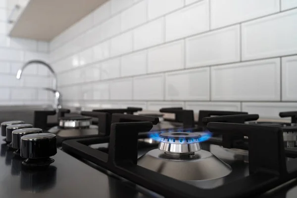Blue flame from a gas stove burner. Stainless steel kitchen surface with cast-iron grill.