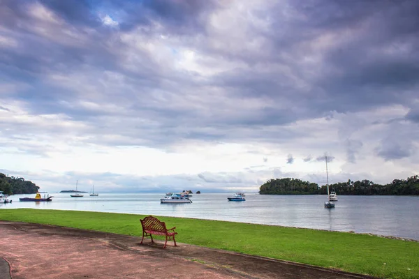 空のベンチ、海、緑の芝生、曇り空、水の輸送 — ストック写真