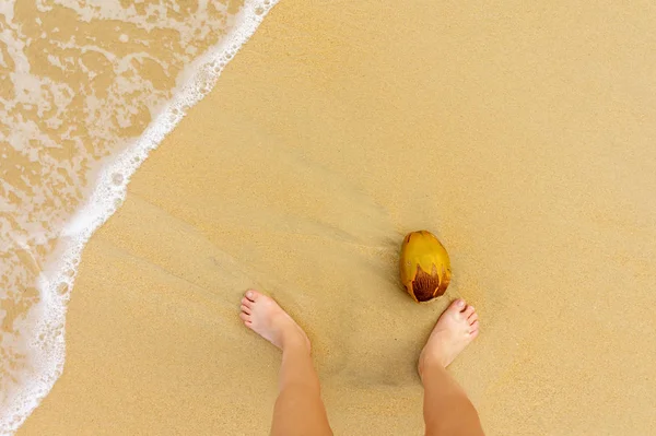 Vista superior de la playa de arena con una ola de mar, pies de hombre y coco — Foto de Stock
