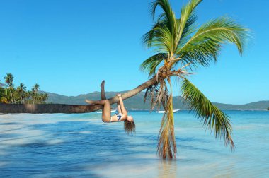 genç kız bikini bir palmiye ağacı üzerinde baş aşağı tırmanıyor. Egzotik tatil kavramı