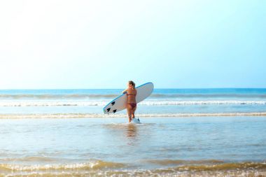 Beyaz sarışın sörfçü kız surfboard ile denize gidiyor