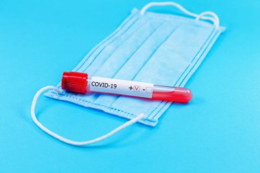 Mavi arka planda koronavirüs kan tüpü testi pozitif olan koruyucu tıbbi maske. Sağlık ve tıbbi konsept. Coronavirus veya COVID-19 koruma kavramı.