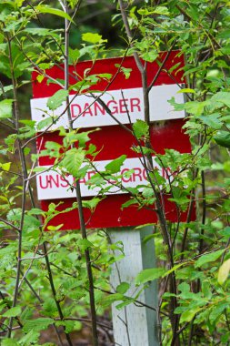 Bir tehlike, kararsız zemin işareti ağaçlar tarafından gizlenmiş