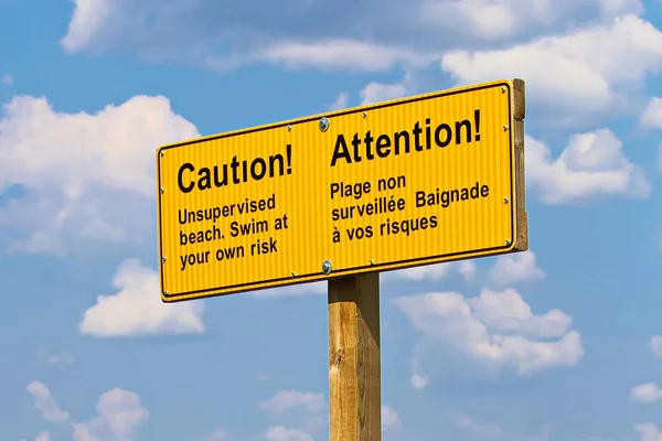 Een gele Let op ongecontroleerde strand teken in Frans en Engels — Stockfoto